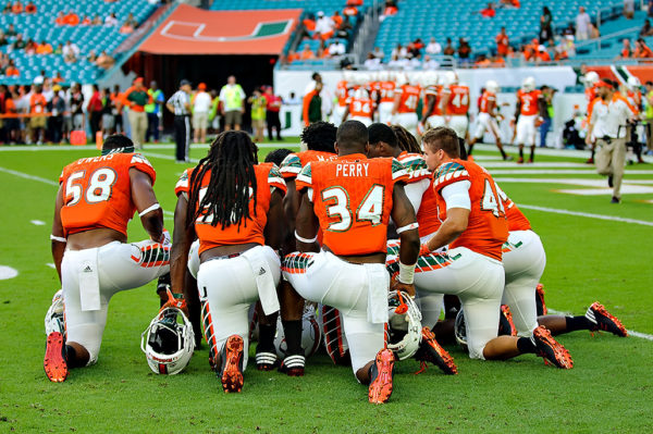 Hurricanes linebackers take a knee to listen to their coach Manny Diaz